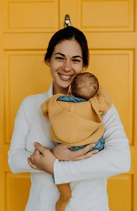 A smiling parent holding their sleeping newborn baby