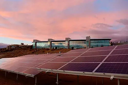 Rows of solar panels in front of a modern building at sunset